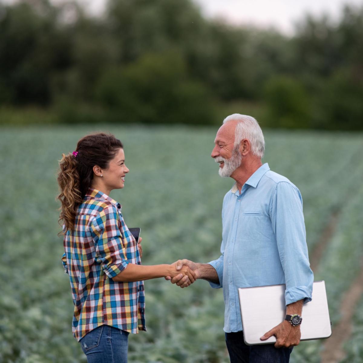 A man and a woman shaking hands in a field of crops.